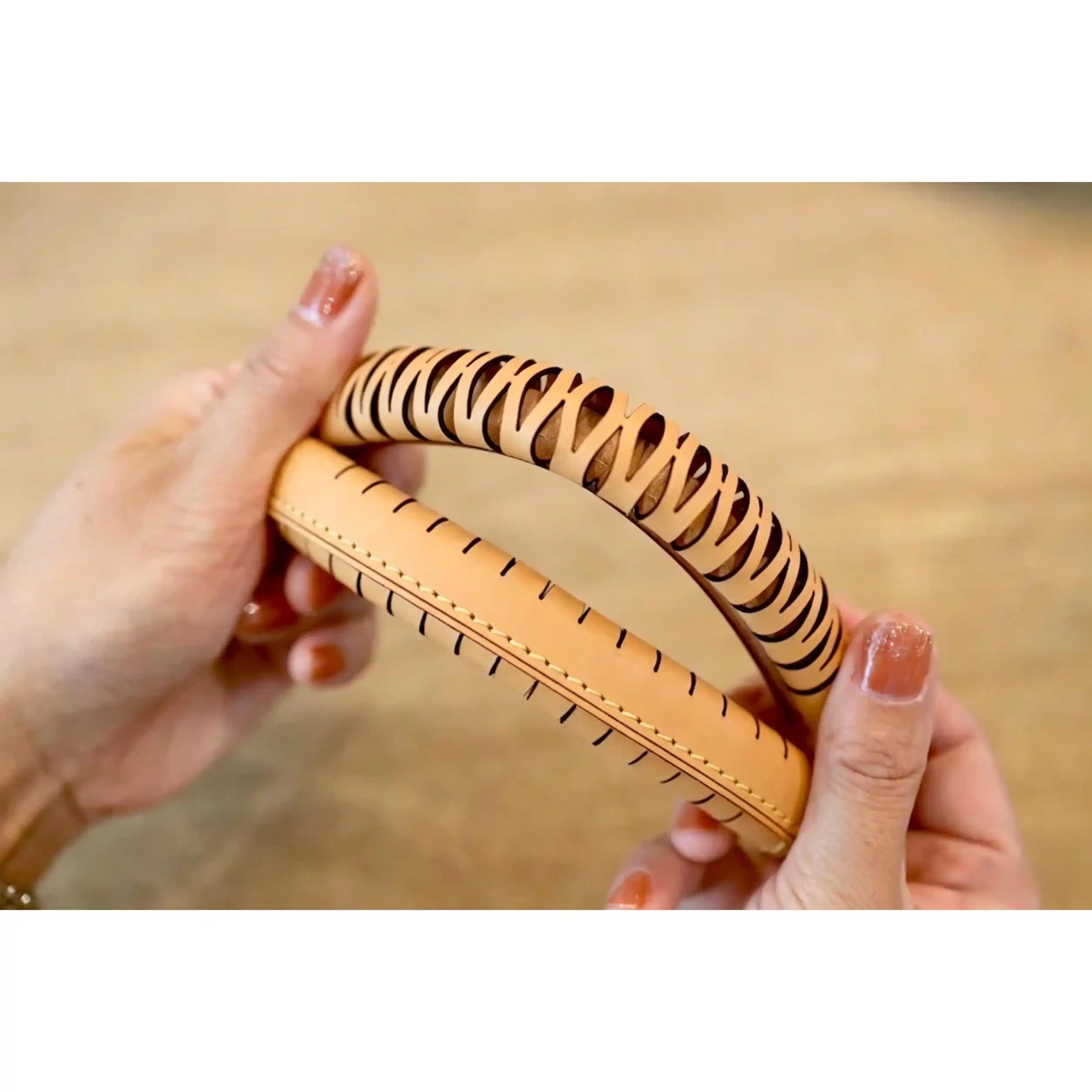 Tan leather bag strap with laser-cut wave pattern and contrast stitching, held in hands