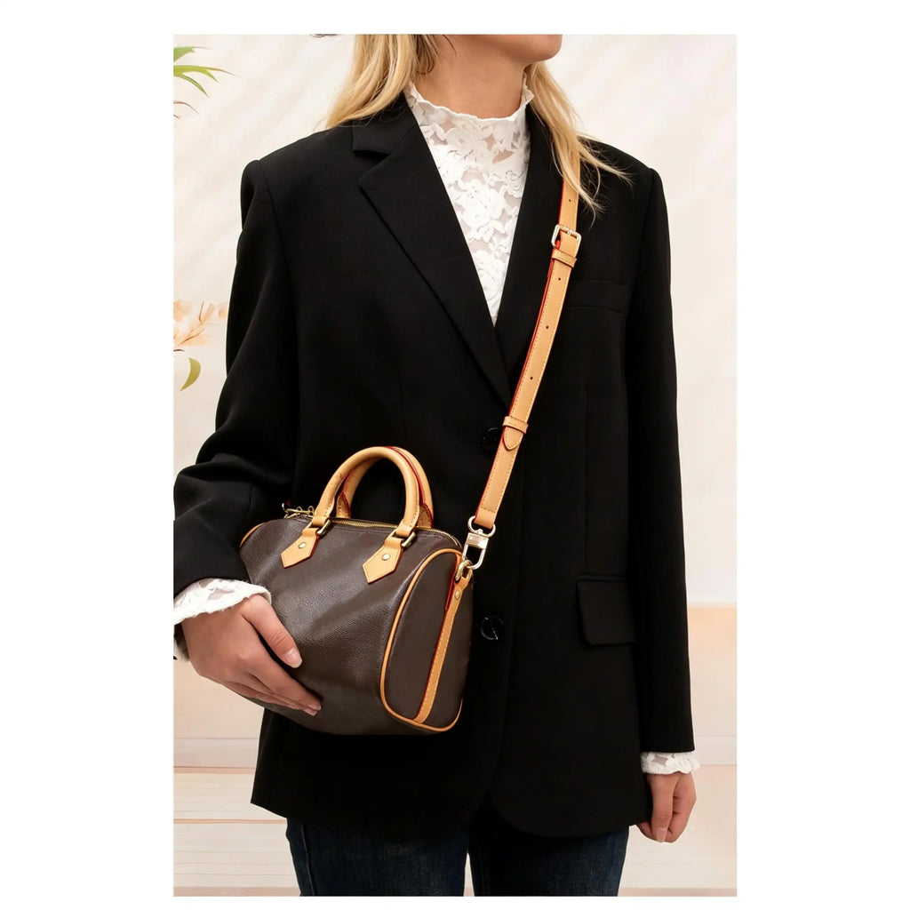 Tan leather bag strap with red stitching, worn crossbody on brown handbag