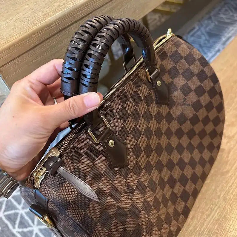 Brown checkered bag with braided leather handles, held in hand